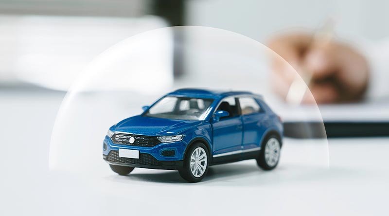 Miniatura de auto azul cubierta por una burbuja protectora, representando la seguridad y respaldo de un seguro automotriz con SGroup